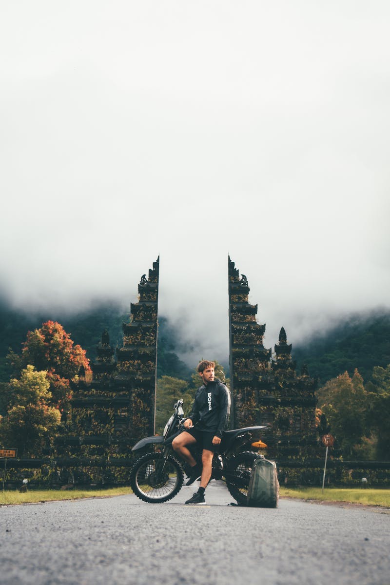 Man posing with motorcycle at iconic Bali temple gate.
