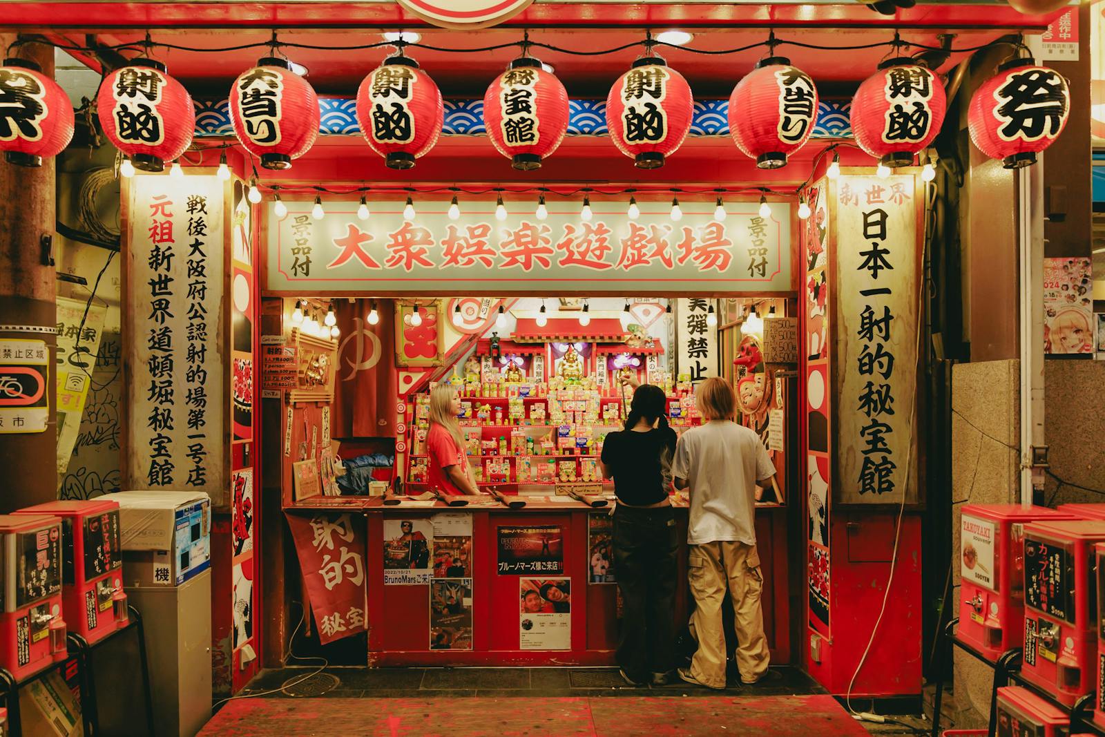 Vibrant Japanese street vendor scene with lanterns and visitors at night, capturing local culture.
