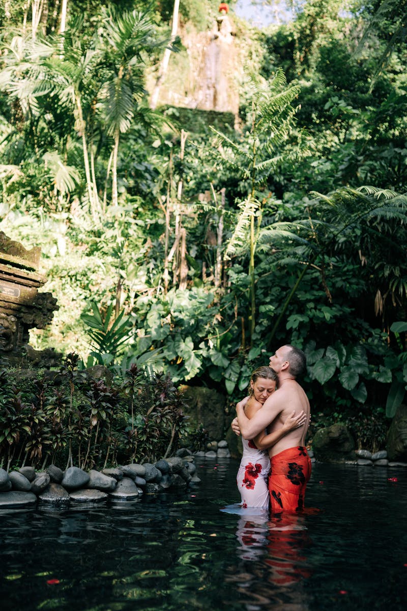 Couple embracing in a serene tropical pond surrounded by lush greenery.