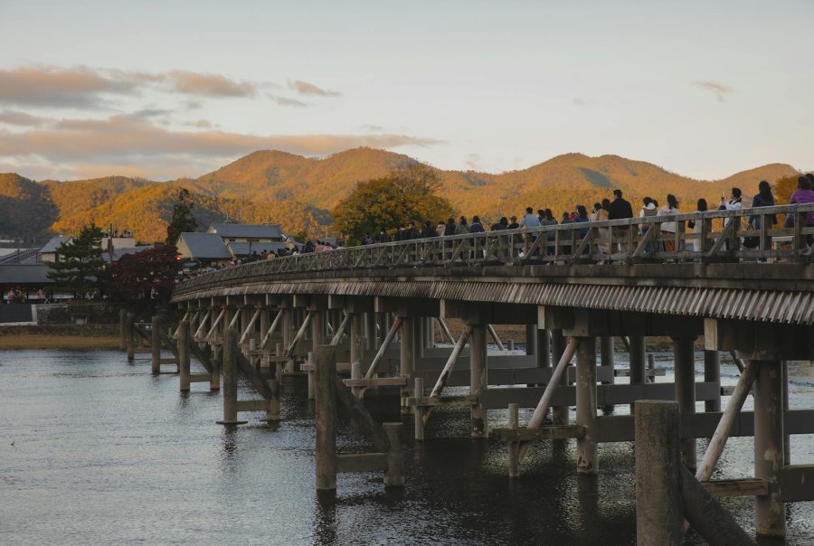 Togetsukyo Bridge over Katsura River in Arashiyama, Kyoto during sunset with tourists enjoying the view.