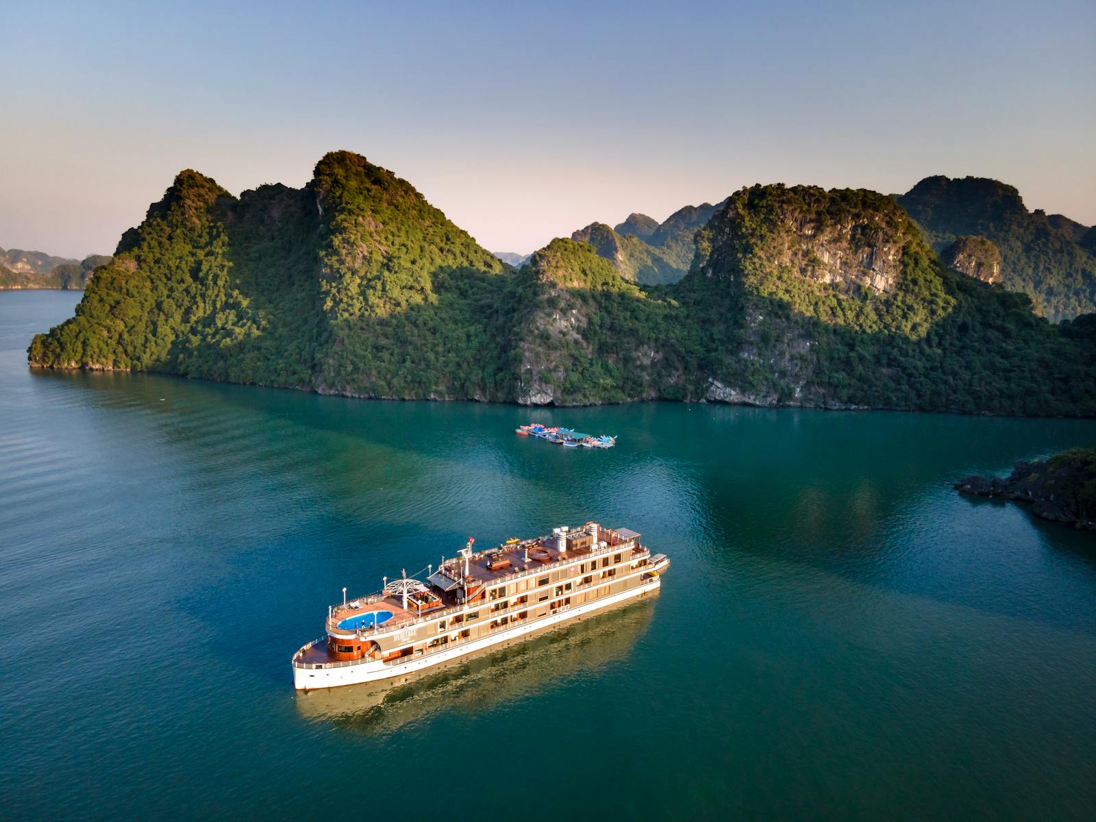 A cruise ship navigates the tranquil waters of Halong Bay with stunning limestone cliffs in the background.